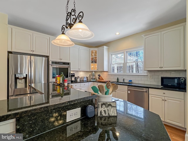 kitchen with appliances with stainless steel finishes, dark stone countertops, hanging light fixtures, white cabinetry, and a sink