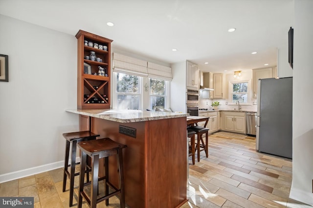 kitchen with appliances with stainless steel finishes, a breakfast bar, a peninsula, light stone countertops, and a sink