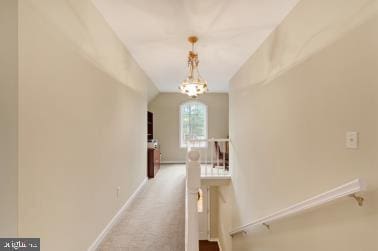 hallway with an upstairs landing, baseboards, vaulted ceiling, carpet, and an inviting chandelier