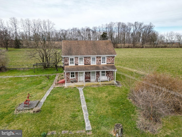 view of front facade with a front lawn, covered porch, roof with shingles, driveway, and an outdoor fire pit