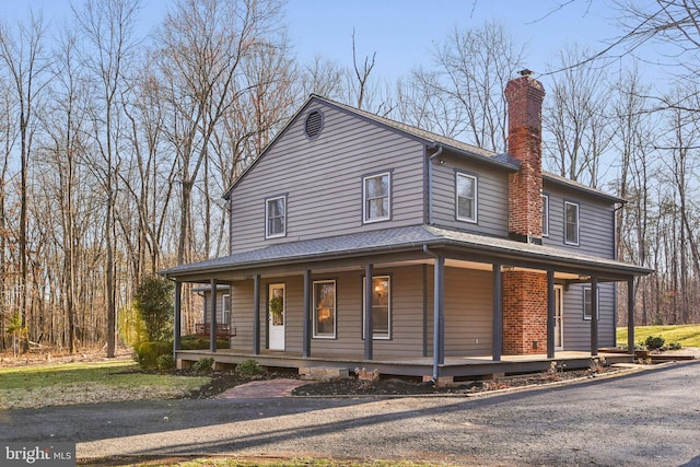 farmhouse-style home featuring covered porch, a chimney, and a shingled roof