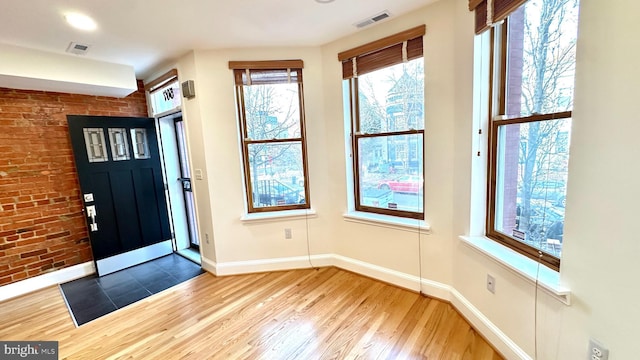 foyer with wood-type flooring and brick wall