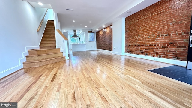 unfurnished living room with brick wall and light wood-type flooring