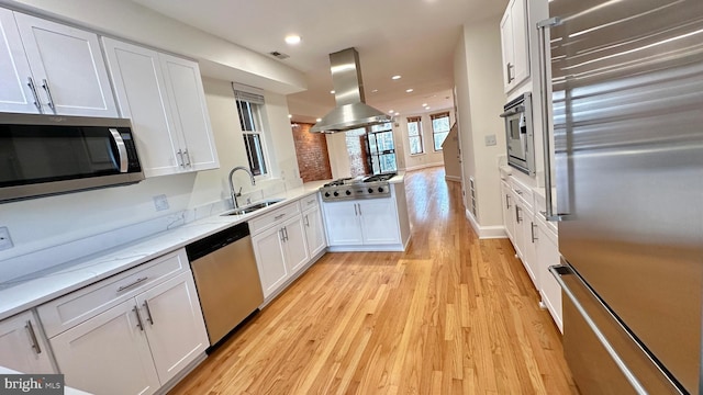 kitchen featuring appliances with stainless steel finishes, sink, light wood-type flooring, white cabinetry, and island range hood