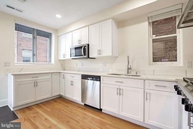 kitchen with stainless steel appliances, light stone counters, white cabinets, light hardwood / wood-style floors, and sink