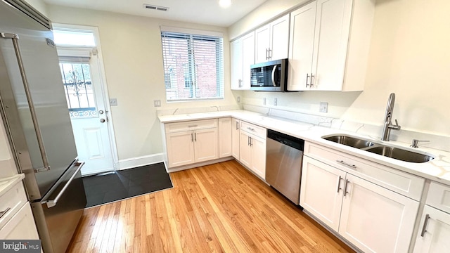 kitchen featuring appliances with stainless steel finishes, light hardwood / wood-style flooring, sink, and white cabinets