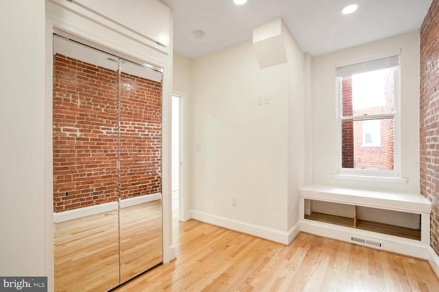 unfurnished bedroom featuring light wood-type flooring and brick wall