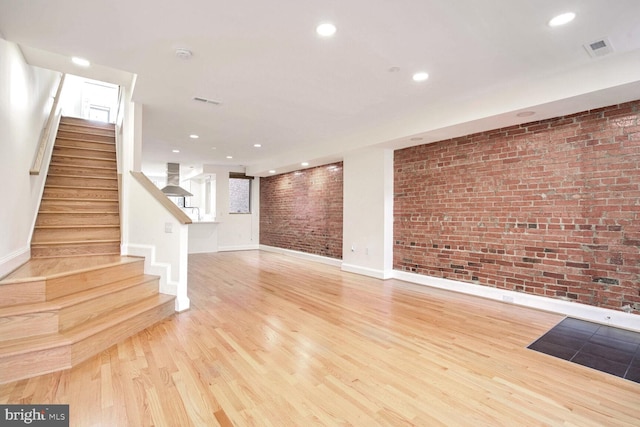 unfurnished living room with light wood-type flooring and brick wall