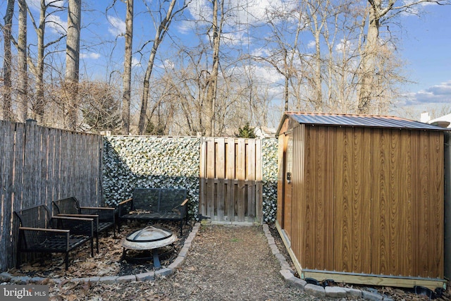 view of yard featuring a storage unit, a fenced backyard, a fire pit, and an outbuilding