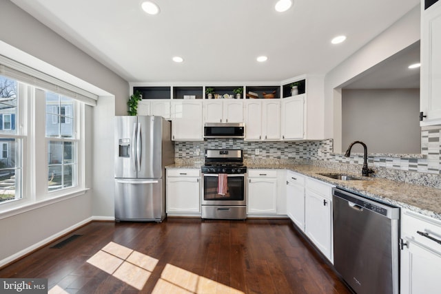 kitchen featuring dark wood-style floors, appliances with stainless steel finishes, light stone countertops, white cabinetry, and a sink