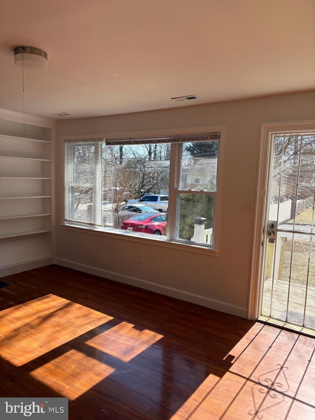 spare room with built in shelves, visible vents, baseboards, and wood finished floors