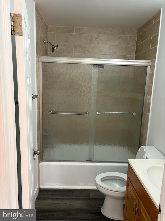 bathroom with enclosed tub / shower combo, vanity, wood finished floors, and toilet