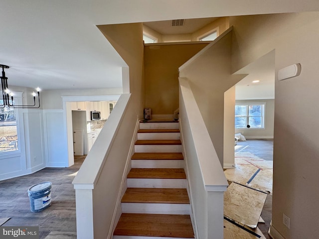 staircase with an inviting chandelier, wood finished floors, a decorative wall, and visible vents
