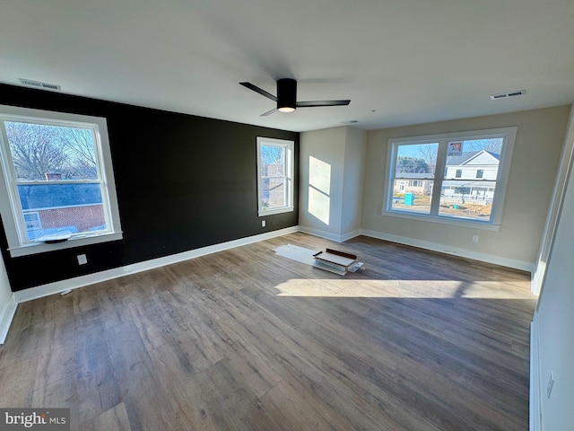 spare room with visible vents, plenty of natural light, a ceiling fan, and wood finished floors