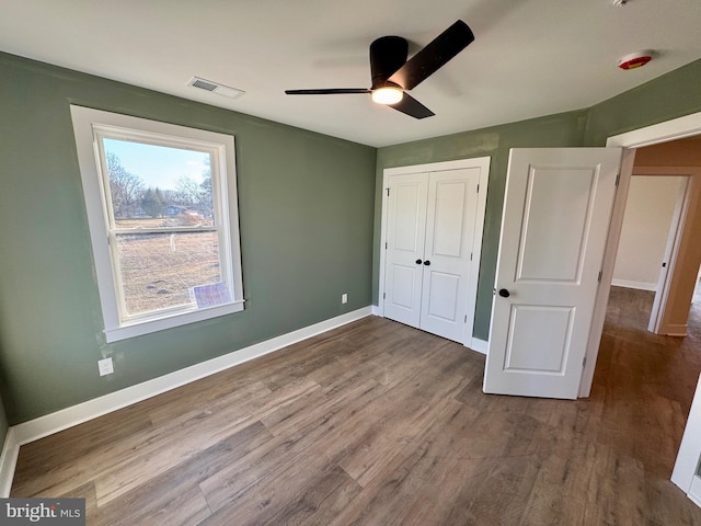 unfurnished bedroom with baseboards, ceiling fan, visible vents, a closet, and wood finished floors