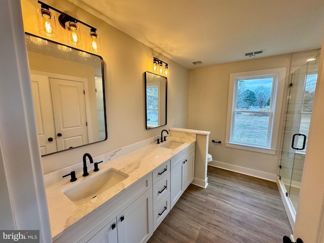bathroom featuring a stall shower, a sink, wood finished floors, visible vents, and double vanity