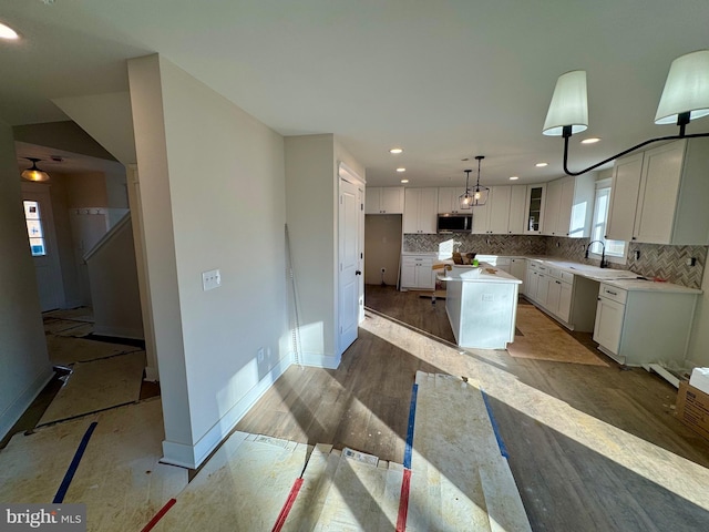 kitchen with tasteful backsplash, stainless steel microwave, white cabinets, a kitchen island, and baseboards