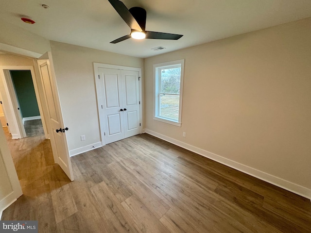 unfurnished bedroom featuring a closet, wood finished floors, baseboards, visible vents, and ceiling fan