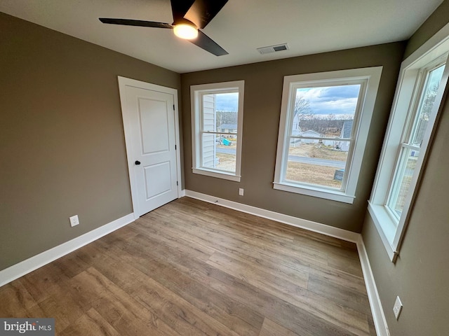 unfurnished room featuring wood finished floors, baseboards, ceiling fan, and visible vents