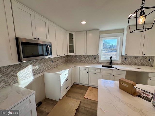 kitchen with light stone counters, backsplash, a sink, stainless steel microwave, and white cabinets