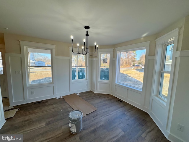 unfurnished dining area with dark wood-style floors, a decorative wall, and a chandelier
