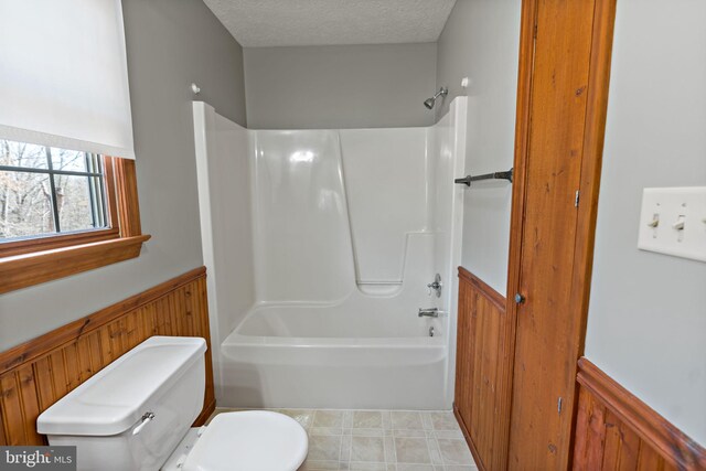 bathroom featuring shower / bath combination, a wainscoted wall, a textured ceiling, and toilet