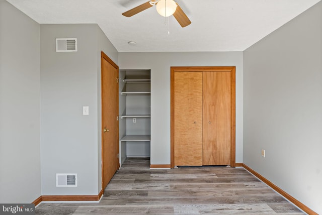 unfurnished bedroom with two closets, baseboards, visible vents, and wood finished floors