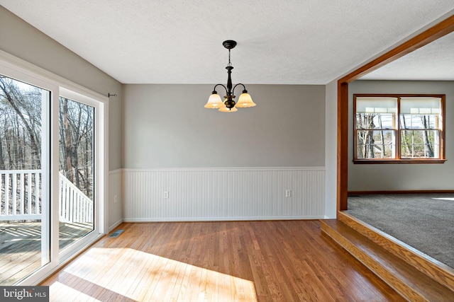 spare room featuring a chandelier, wainscoting, plenty of natural light, and hardwood / wood-style floors