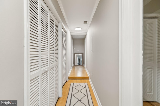 corridor with light wood-type flooring, visible vents, baseboards, and crown molding