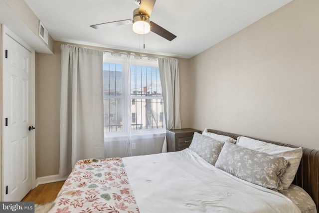 bedroom with a ceiling fan, baseboards, visible vents, and wood finished floors