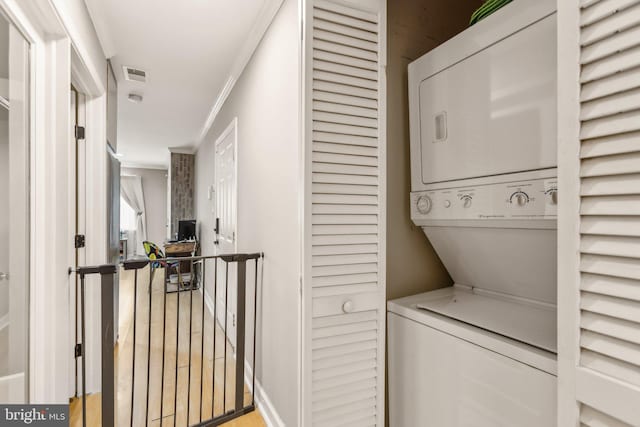 laundry room featuring laundry area, visible vents, stacked washer / dryer, ornamental molding, and wood finished floors