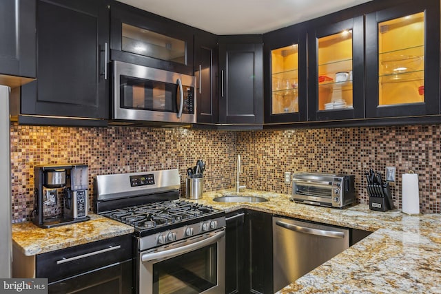 kitchen featuring a toaster, stainless steel appliances, backsplash, glass insert cabinets, and a sink