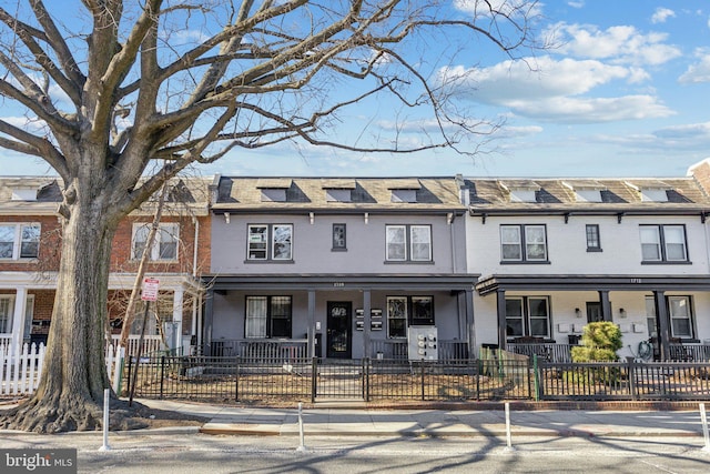 townhome / multi-family property featuring a fenced front yard, brick siding, and mansard roof