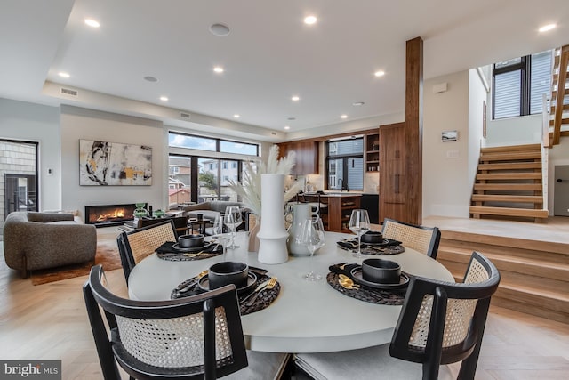 dining area featuring a warm lit fireplace, stairway, visible vents, and recessed lighting