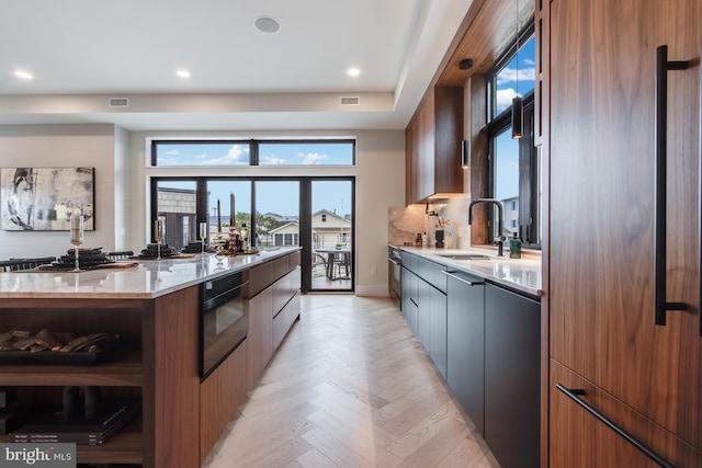 kitchen featuring visible vents, modern cabinets, oven, light stone countertops, and a sink