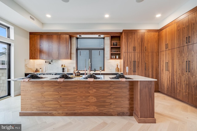 kitchen featuring a kitchen island with sink, light countertops, brown cabinetry, and visible vents