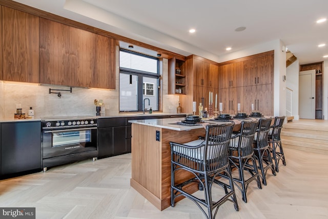 kitchen featuring electric range, tasteful backsplash, brown cabinetry, modern cabinets, and a kitchen bar