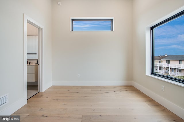 empty room with light wood-style flooring, visible vents, and baseboards