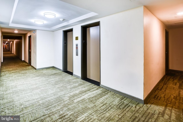 corridor featuring a raised ceiling, elevator, and baseboards