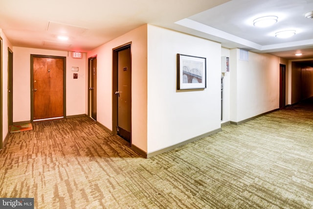 hallway with a tray ceiling, baseboards, and carpet flooring