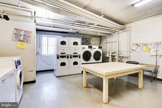 shared laundry area with concrete block wall, light floors, stacked washer / dryer, and independent washer and dryer