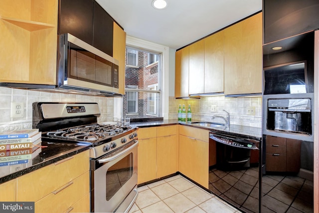 kitchen featuring backsplash, dark stone countertops, stainless steel appliances, and a sink