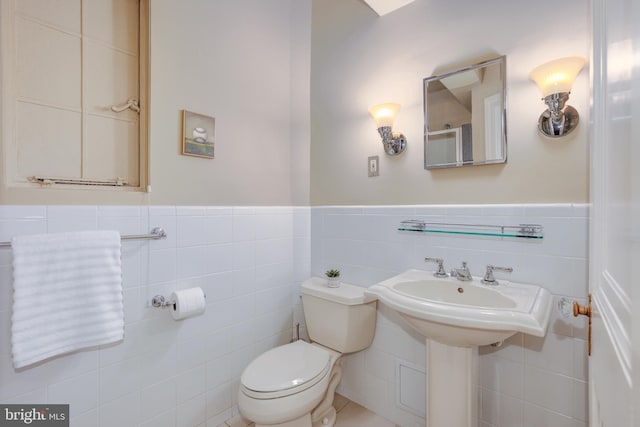 half bath featuring wainscoting, tile walls, and toilet