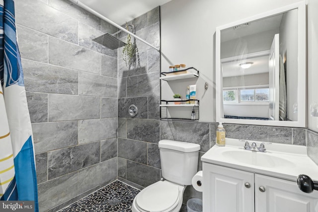 bathroom with toilet, a tile shower, vanity, and tile walls