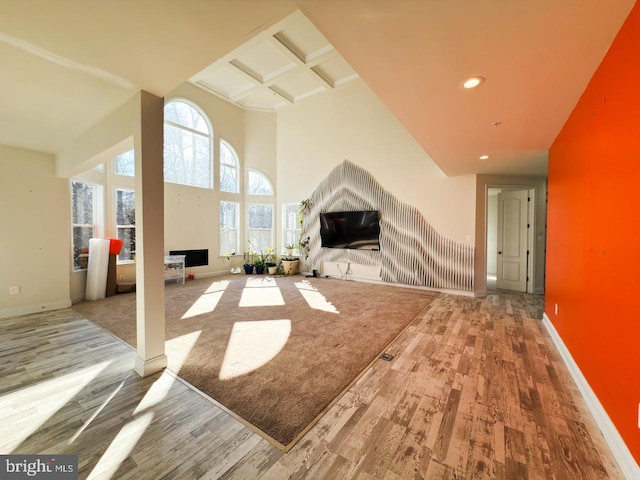 living room with baseboards, coffered ceiling, wood finished floors, and a towering ceiling