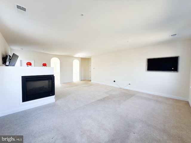 unfurnished living room with arched walkways, visible vents, light carpet, and a glass covered fireplace