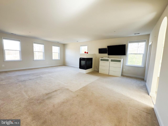 unfurnished living room featuring baseboards, a multi sided fireplace, and light carpet