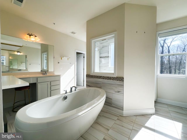 bathroom with visible vents, a soaking tub, tile walls, and vanity