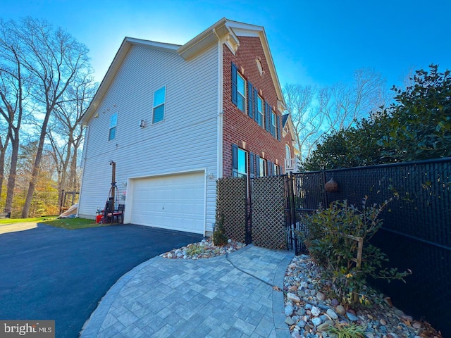 view of side of home with brick siding, driveway, a garage, and fence