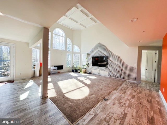 unfurnished living room with a towering ceiling, wood finished floors, baseboards, and coffered ceiling